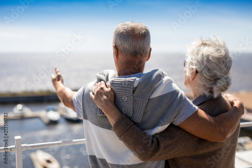 Senior man pointing at beach while embracing his wife by seaside