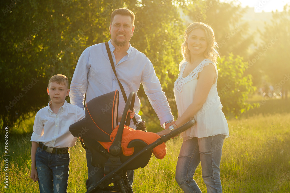 Obraz premium active big happy family father, mother, son and baby in stroller walking in the park