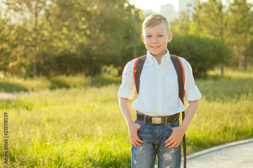 stylish and young schoolboy in a white shirt and jeans with a backpack in the park