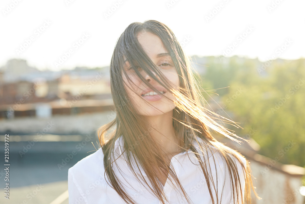 Young carefree woman with dark long hair looking at camera with toothy smile on sunny morning Young carefree woman with dark long hair looking at camera with toothy smile on sunny morning