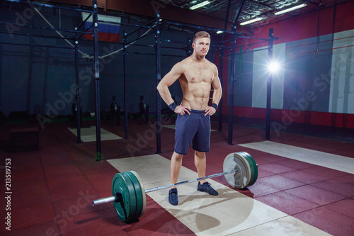 portrait of a muscular man workout with barbell at gym. stands near the bar, resting.