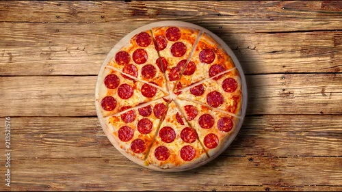 A video of the background pepperoni pizza on a wooden table. Footage.