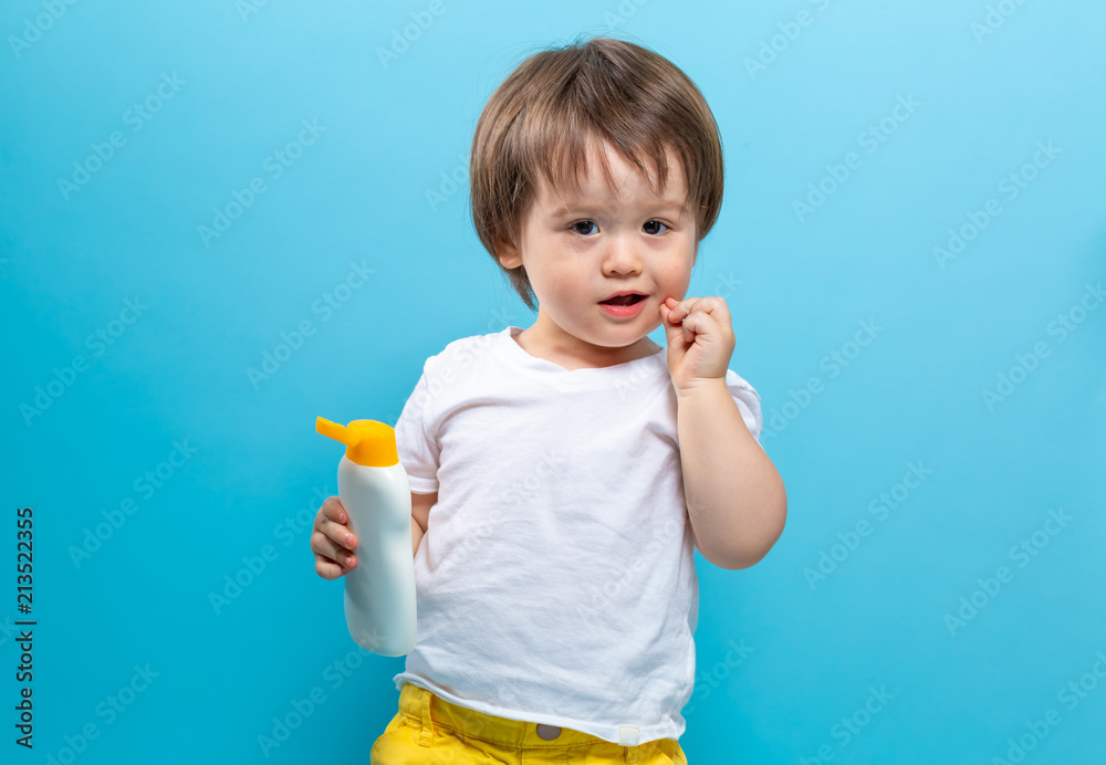 Toddler boy with a bottle of sunblock on a blue background Toddler boy with a bottle of sunblock on a blue background
