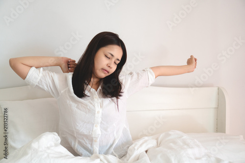 Young beautiful asian woman waking up in bed and stretching in bed in morning.