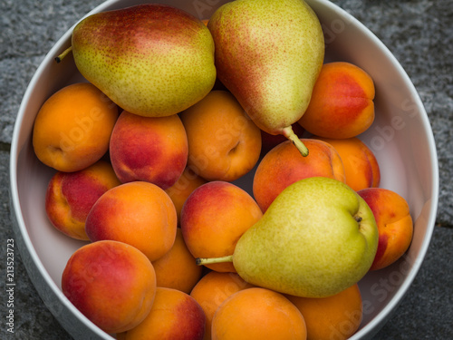 Ripe apricots and pears in a white bowl. Fresh fruits. Top view of a close-up.