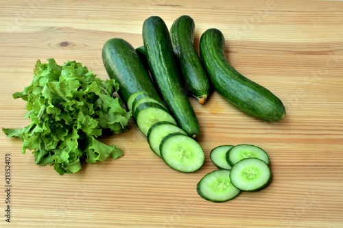 Fresh cucumbers and salad leaves on a wooden table.