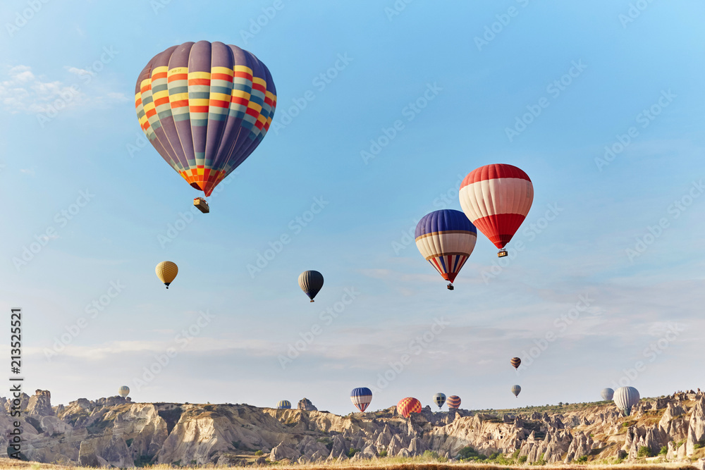Fototapeta premium Large number of balloons fly in morning in the sky in rays of the dawn sun. Balloons balloons in the sky in the clouds above the mountains. Main attraction of Cappadocia, Turkey. Fabulous view