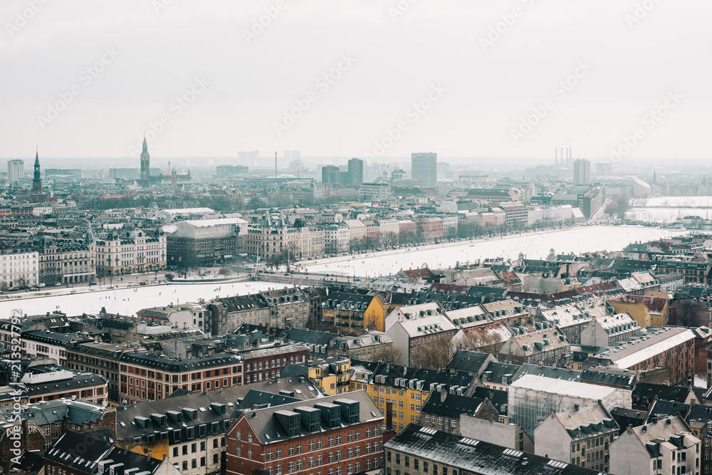 Central Copenhagen skyline view in winter. Cloudy weather and snow on the rooftops. People walking on the frozen lakes.