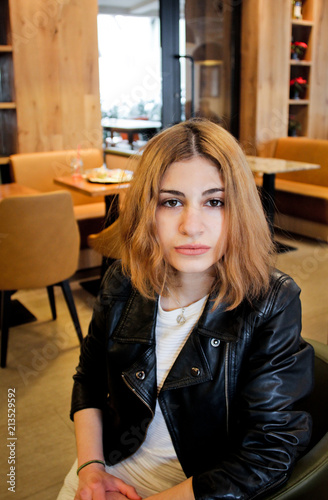 Pretty girl with cup of coffee inside cafe. Attractive woman wear in black leather jacket. Cheerful lady enjoy and relax.