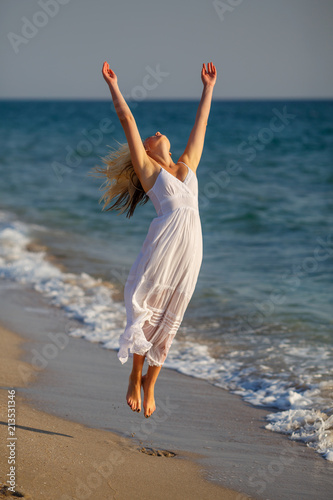 beautiful happy woman in white dress jumping up on the beach on a Sunny day