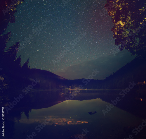 Mountain lake Synevir at night with starry sky and reflections in the water. Natural outddors travel dark background. Carpathian, Ukraine