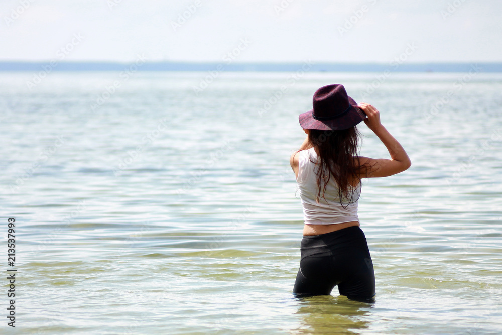 Beautiful sexy girl back side on the beach standing in the water in a hat