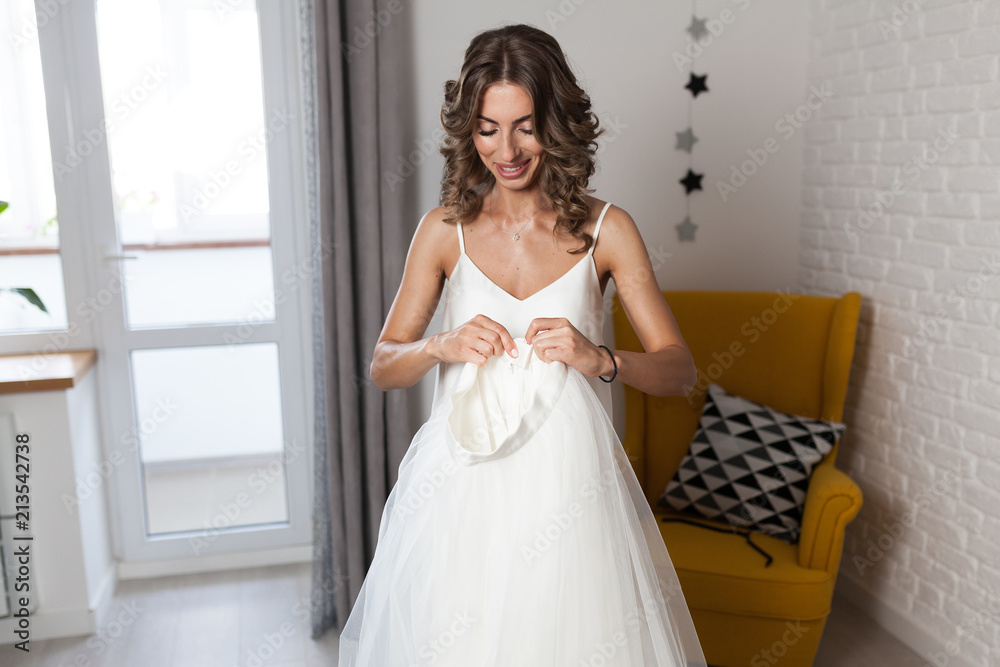 A beautiful curly-haired girl, a future bride measuring a wedding dress in her house before the wedding. A beautiful curly-haired girl, a future bride measuring a wedding dress in her house before the wedding.