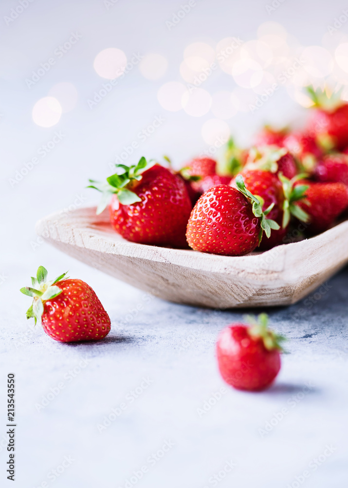 Frische Erdbeeren in einer Holzschale und kleinem Lichtbokeh im Hintergrund Frische Erdbeeren in einer Holzschale und kleinem Lichtbokeh im Hintergrund