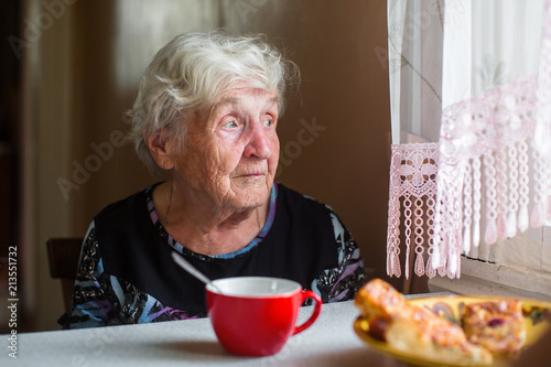 An elderly woman near the window with a Cup of tea.