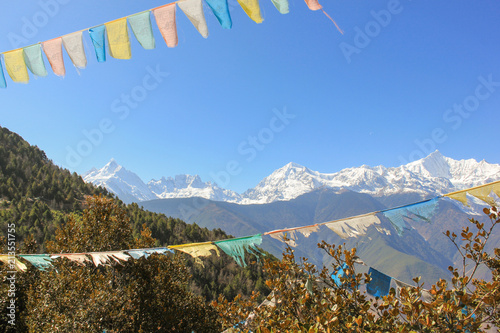 Tibetan prayer flags among trees with Meili Xue Shan mountain range on the background in Deqin town, Yunnan province, China. Freedom symbol, nature landscape concepts photo