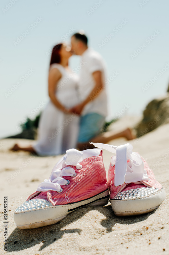 Naklejka premium photo shoot of a pregnant couple on the beach. the girl has red hair . small sneakers pink