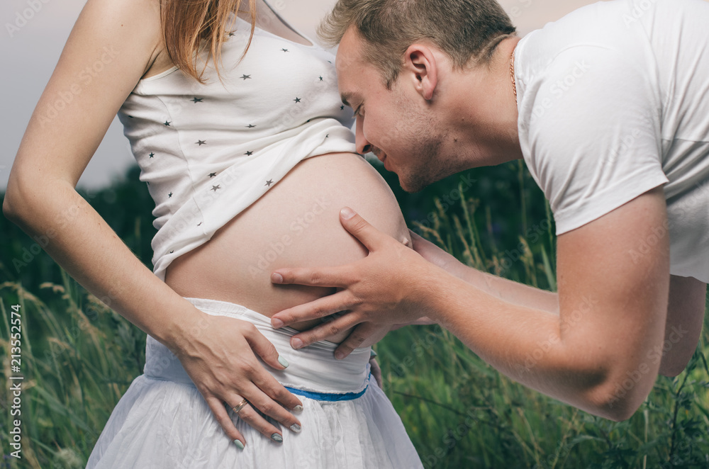 pregnant woman , expectant mother . dressed in white, family photo shoot at sunset in a field . husband listening to pregnant belly pregnant woman , expectant mother . dressed in white, family photo shoot at sunset in a field . husband listening to pregnant belly