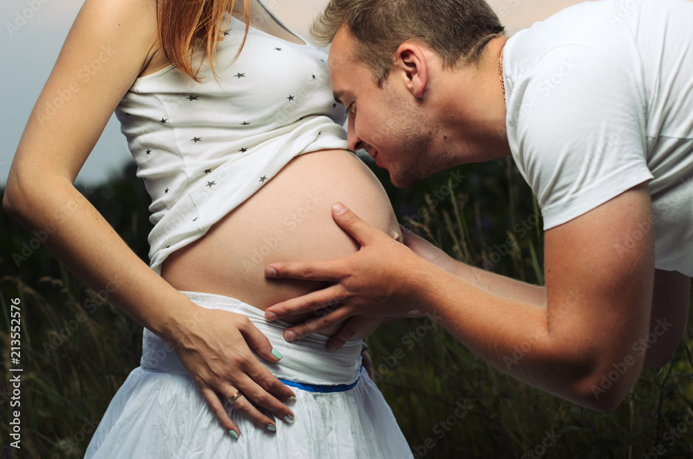 pregnant woman , expectant mother . dressed in white, family photo shoot at sunset in a field . husband listening to pregnant belly pregnant woman , expectant mother . dressed in white, family photo shoot at sunset in a field . husband listening to pregnant belly