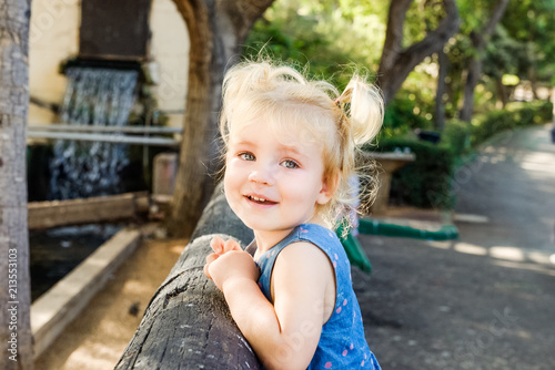 Close up Portrait of little blondy toddler Girl Smiling at Camera. Happy kid walking outdoors in the park or zoo. Family recreation, leasure time concept. Selective focus. Copy space.