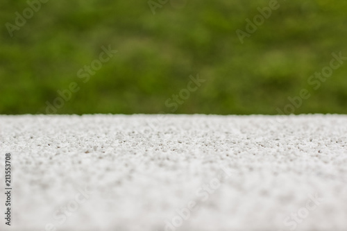soft focus white concrete surface foreground texture and unfocused green grass background concept with empty space for copy or text
