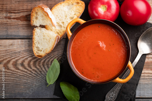 Homemade tomato soup with Basil, toast and olive oil on a wooden table. Prepared a vegetarian dish on a dark background. Top view with copy space
