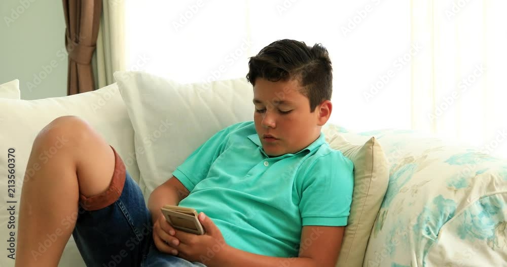 Preteen boy laying sofa with smartphone texting message or playing game at home. Technology, internet communication and people concept Preteen boy laying sofa with smartphone texting message or playing game at home. Technology, internet communication and people concept