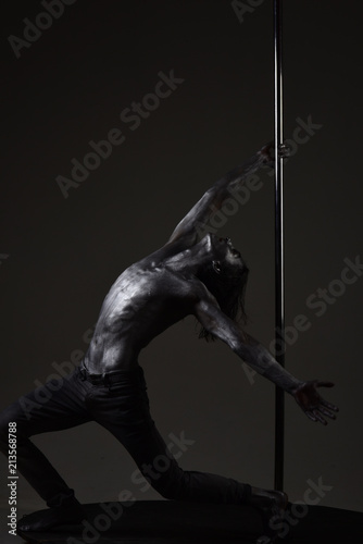 Sexy macho with metal skin. Athletic man make acrobatic elements on pylon. Pole dance sport. Muscular man with silver body art dancing on pylon. Moving to his goal. dancer workout on pole. Freedom