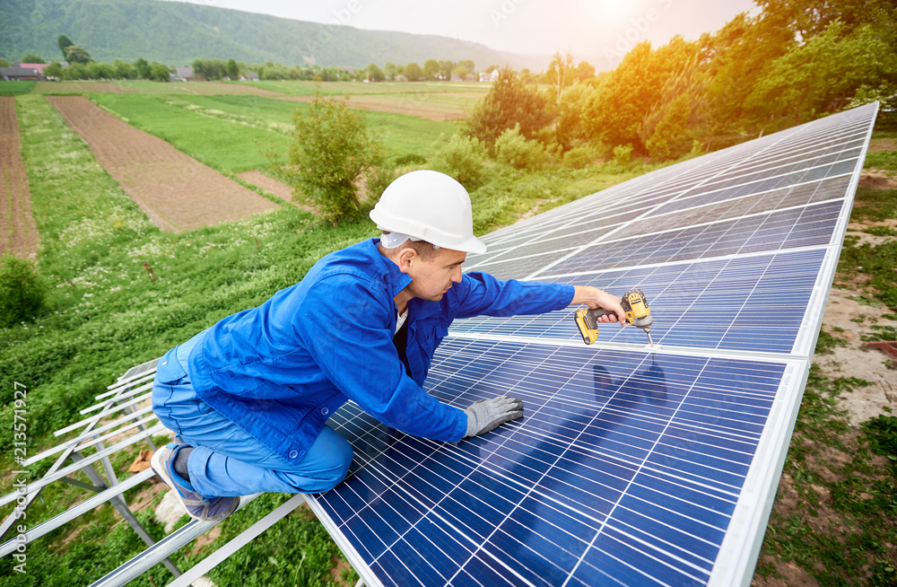 Construction worker connects photo voltaic panel to solar system using screwdriver. Professional installing and construction of solar system, alternative energy and financial investment concept.