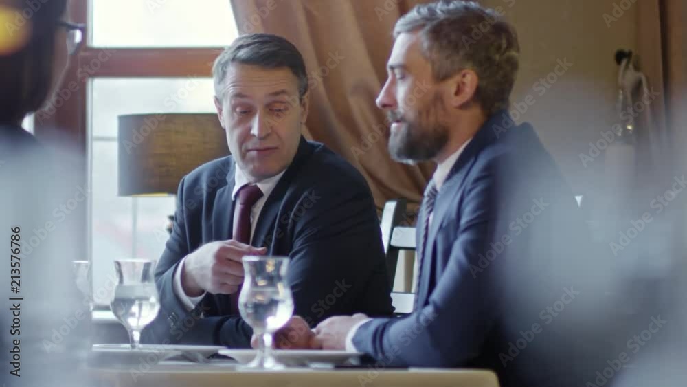 Two mature businessmen sitting at table in cafe or restaurant and having conversation at meeting with colleague Two mature businessmen sitting at table in cafe or restaurant and having conversation at meeting with colleague