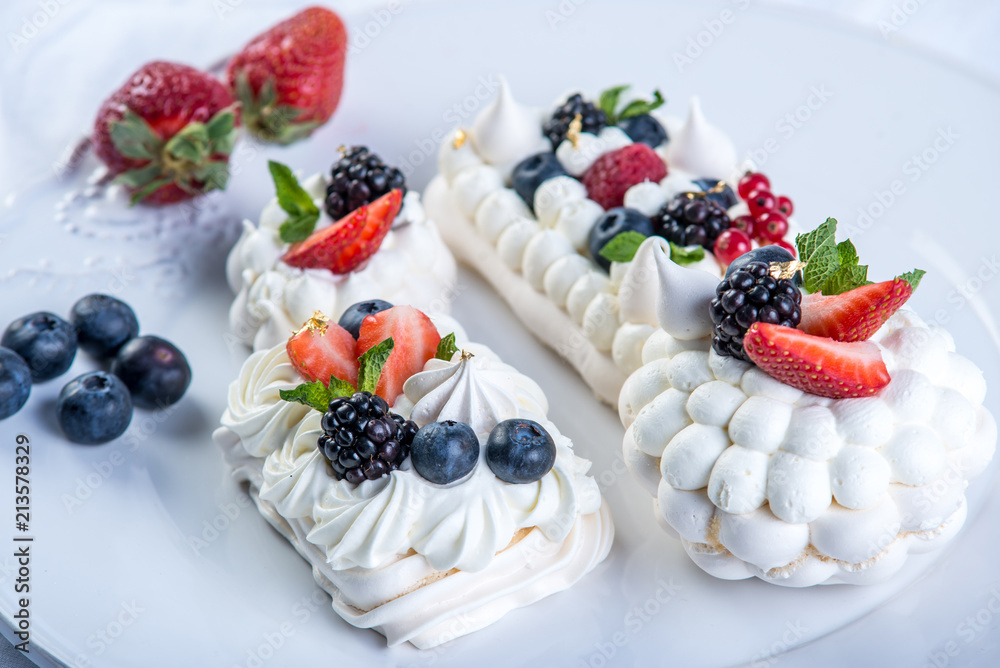 Delicate white meringues with fresh berries on the plate on white background. Dessert Pavlova close-up. Wedding cake.
