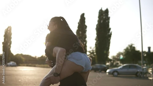 Young couple having fun on summer on an empty parking zone with boyfriend giving piggyback ride to girlfriend. Smiling, cheerful young people. Sun shining