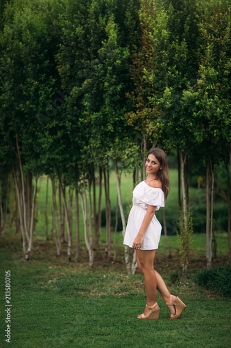 young and pretty girl in white dress in a summer city standing near the tree