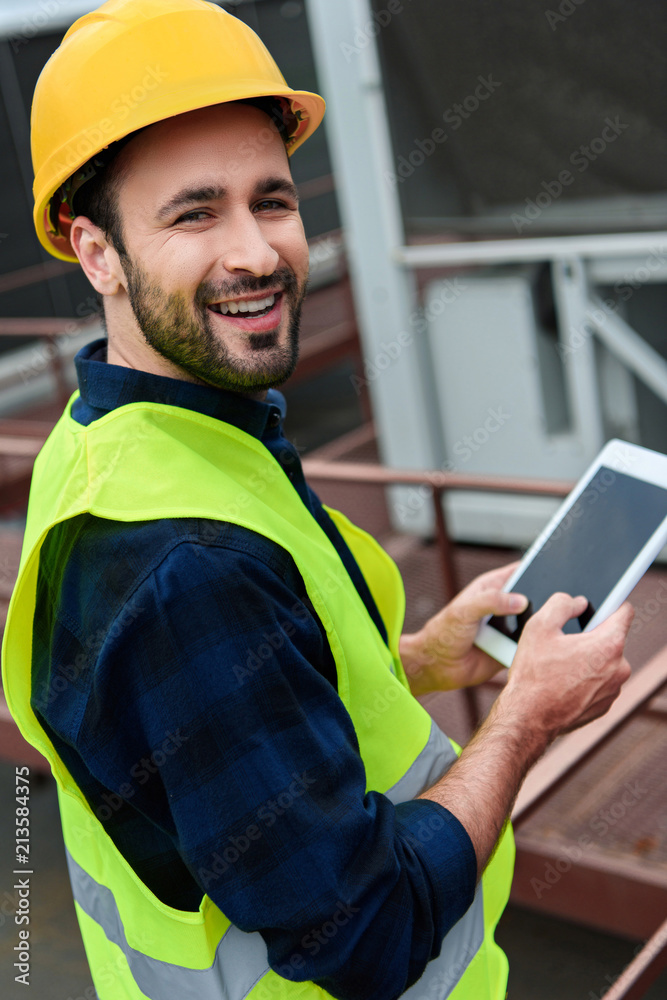 cheerful construct worker in safety vest and helmet using digital tablet with blank screen cheerful construct worker in safety vest and helmet using digital tablet with blank screen
