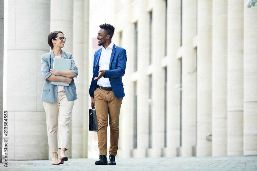 Happy excited office colleagues in stylish outfits talking about work when  walking over street in summer Stock Photo