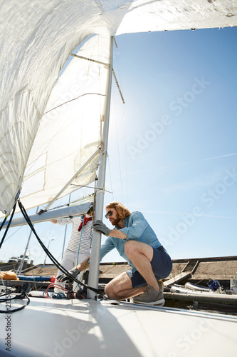 Serious busy men in casual clothing tying ropes together and examining sail boat before sailing in summer