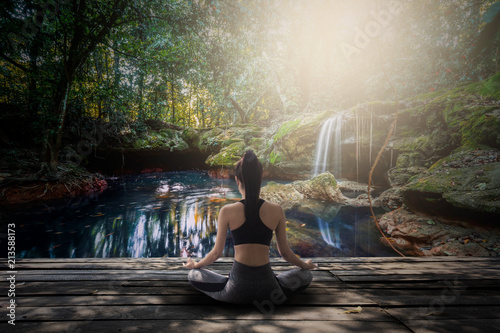young women meditate while doing yoga at the waterfall in the forest