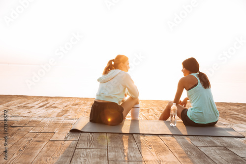 Two sports women friends outdoors on the beach sitting talking with each other