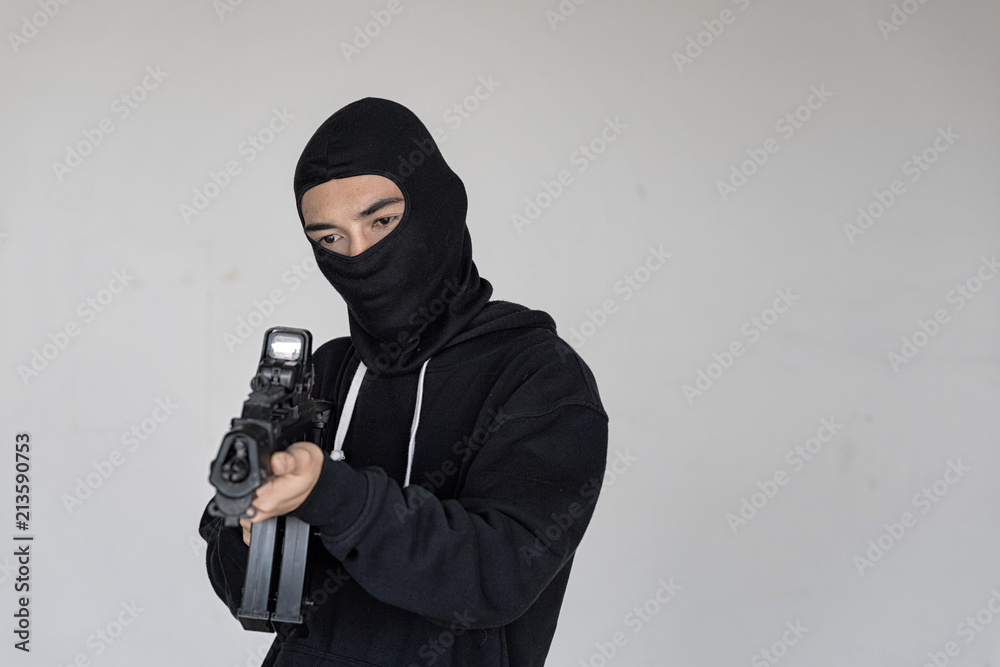 Black masked Robber in the black long sleeve shirt is  aiming the machine gun in his hand. He look at outside. Selective focus at his face.