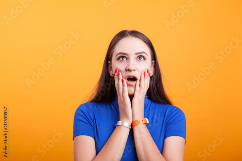 Surprised and amazed girl hold her cheecks in studio over yellow background