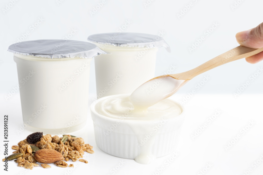Hand's woman holding wooden spoon with healthy flavored yogurt in plastic cup and ceramic bowl with cereal and isolated on the white background. With copy space for your text. Hand's woman holding wooden spoon with healthy flavored yogurt in plastic cup and ceramic bowl with cereal and isolated on the white background. With copy space for your text.