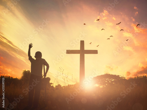 Concept conceptual black cross religion symbol silhouette in grass over sunset or sunrise sky