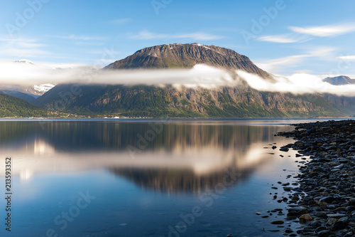 Sunrise illuminates the mountain which is reflected on the surface of the water in Skibotn, Norway. photo