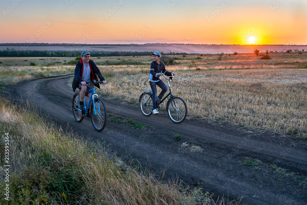 Obraz premium father and son ride a bike in the country on the field in the evening