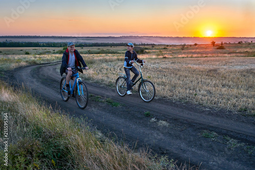 father and son ride a bike in the country on the field in the evening