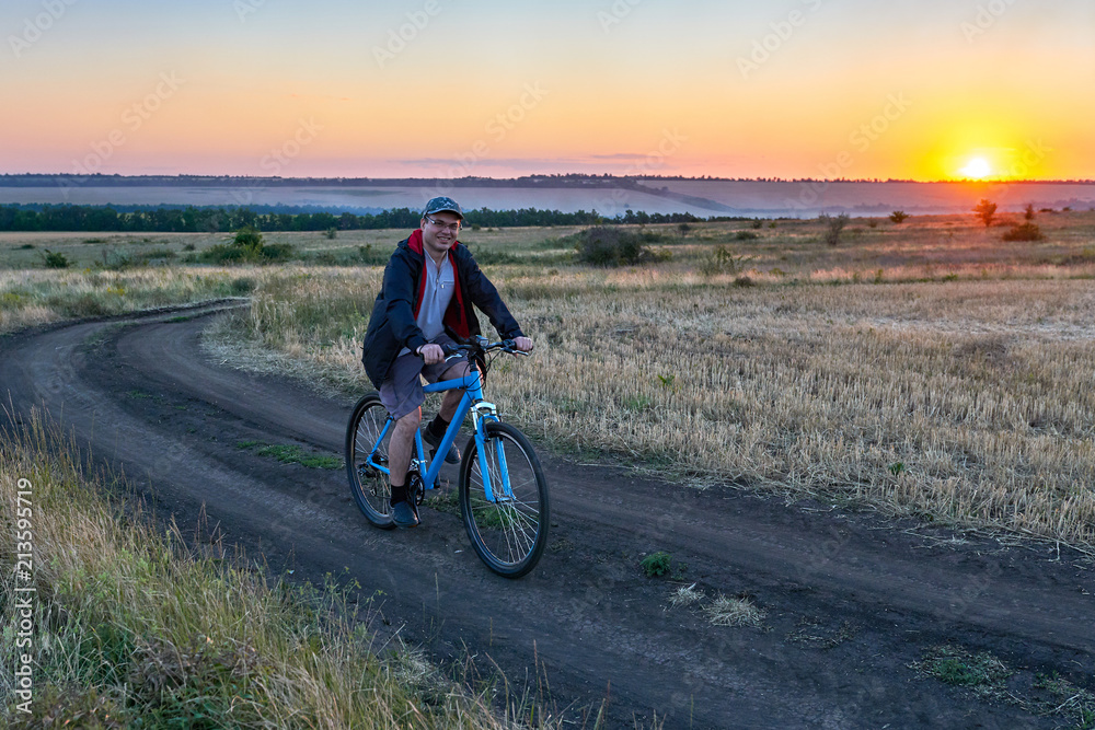 man ride a bike in the country on the field in the evening