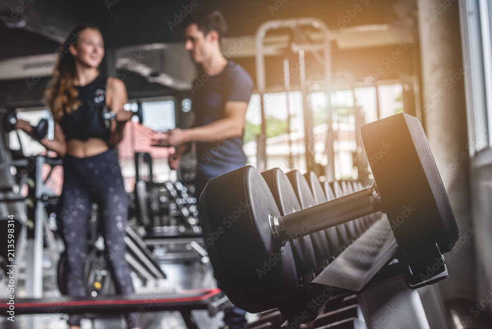 Cinematic tone of young attractive fitness woman exercise with dumbbell by trainer in gym. Cinematic tone of young attractive fitness woman exercise with dumbbell by trainer in gym.