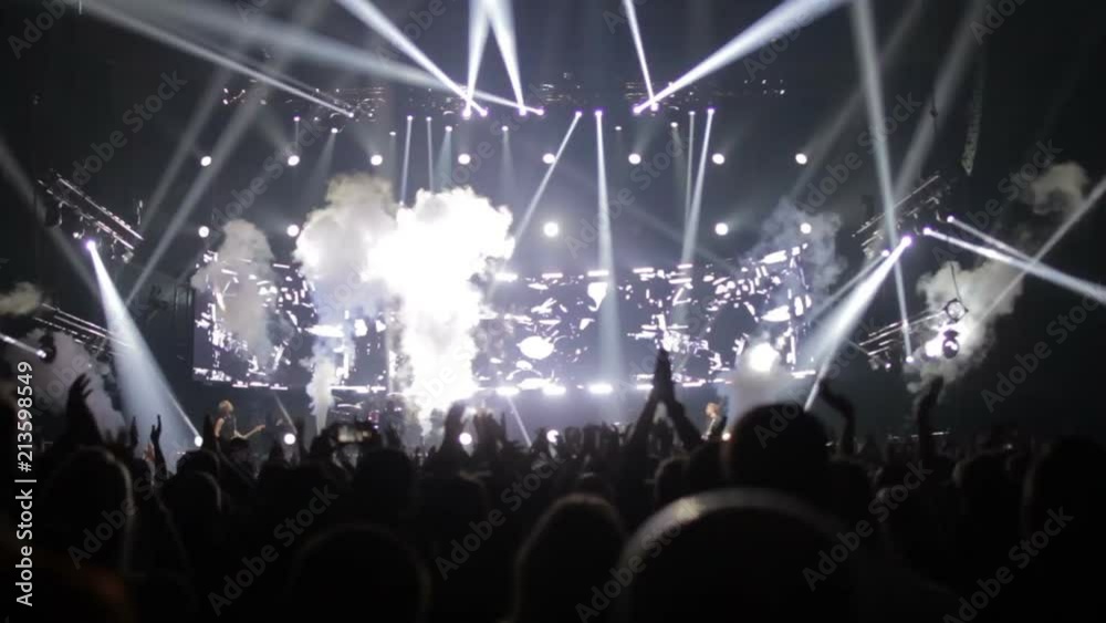 The audience at the concert waving their hands, on the stage a light show, a concert