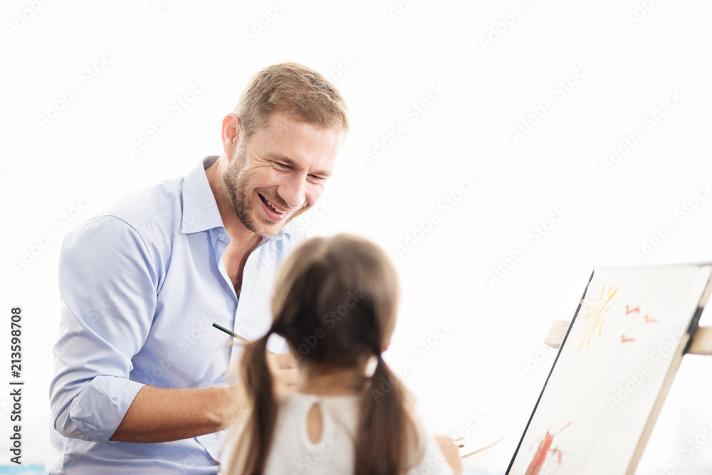 Obraz premium Young father teaching daughter to draw a picture. Happy time together. Setup studio shooting. Selective focus at father.