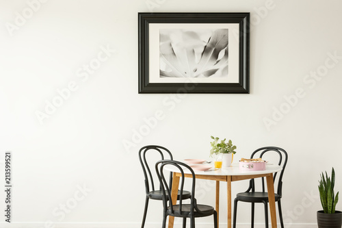 Real photo of a laid dining table with black chairs and painting on an empty wall. Place your graphic © Photographee.eu